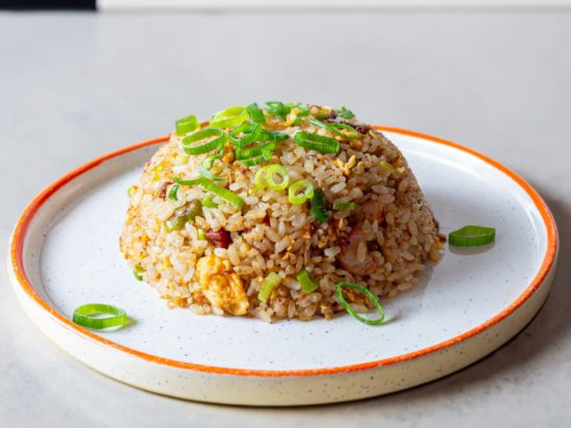 An Asian rice dish garnished with spring onions sits on a plate, shaped into a dome