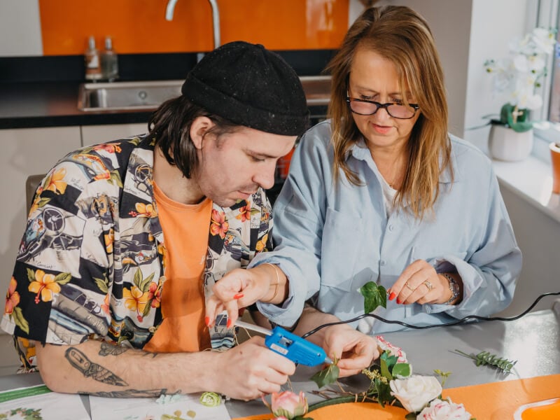 A mum and son work on a floral wreath together.
