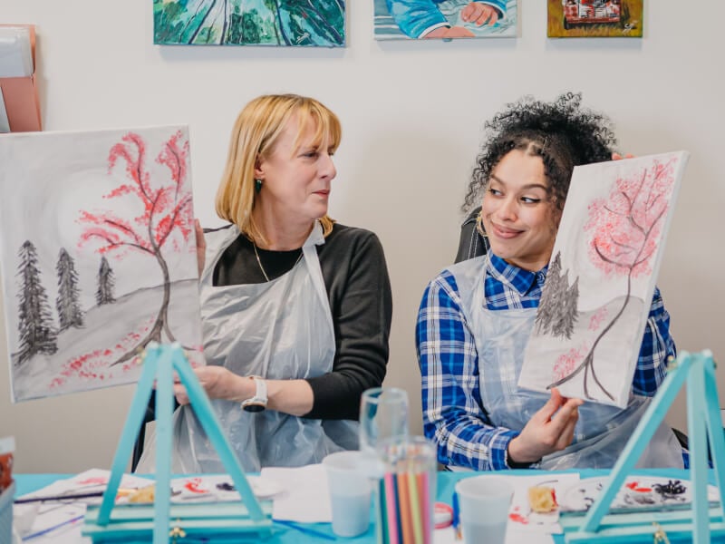 A mum and daughter show off the paintings they made in an art class.