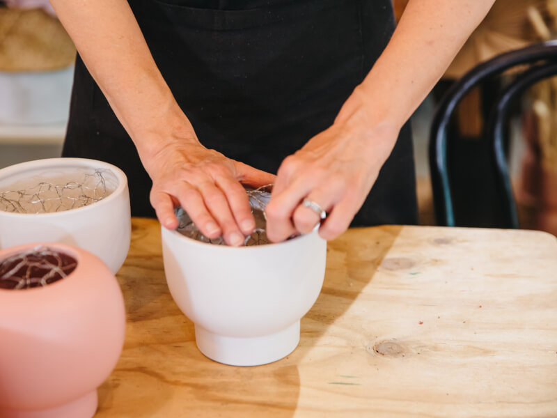 Person packing a decorative plant pot with potting soil