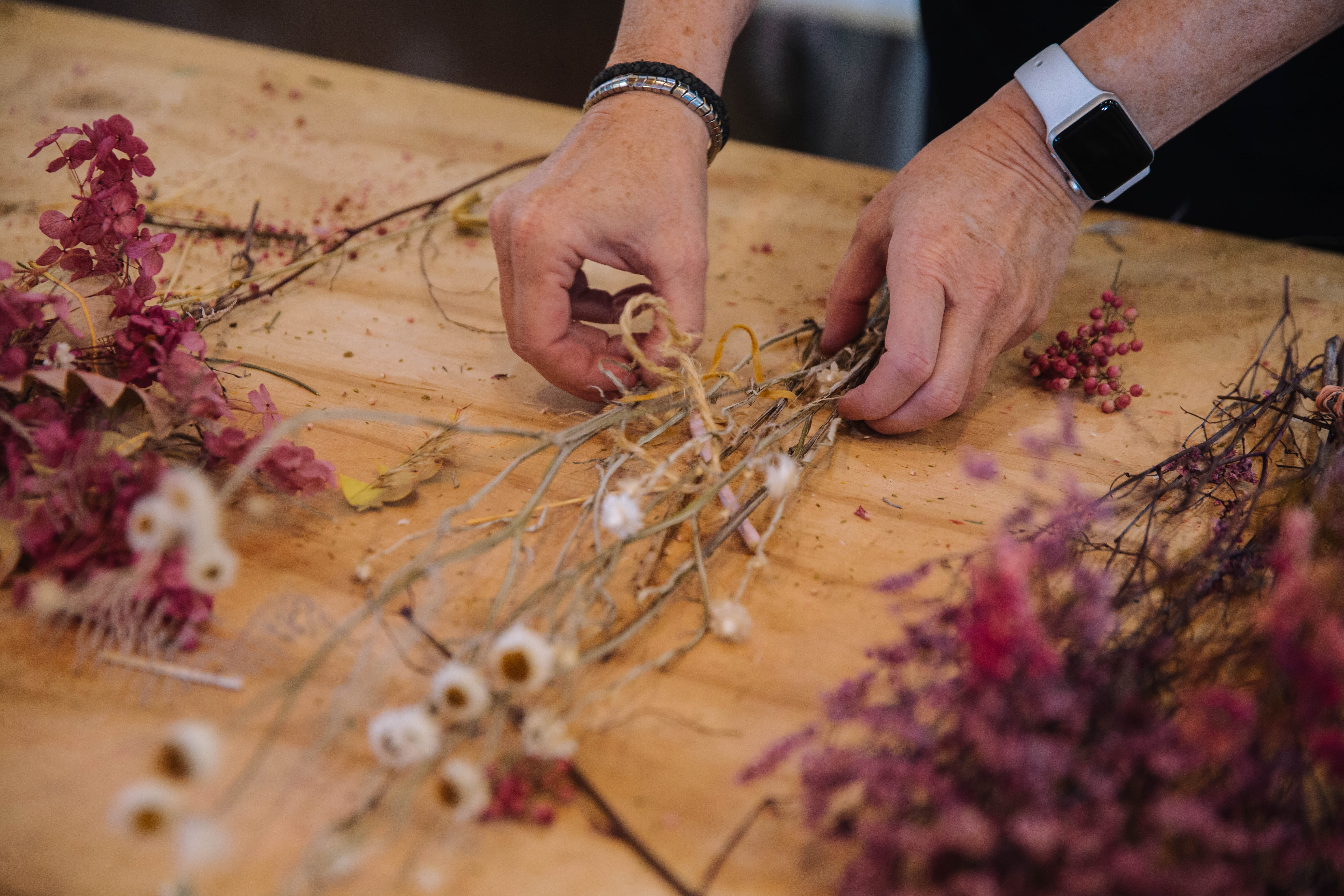 Person arranging dried flowers on a wooden table