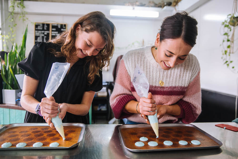 Two women pipe out macroon shells in a baking class.