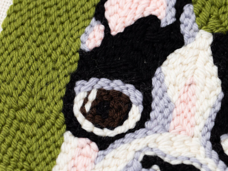 A close up image of an embroidered pug in green, purple, black and white stitching