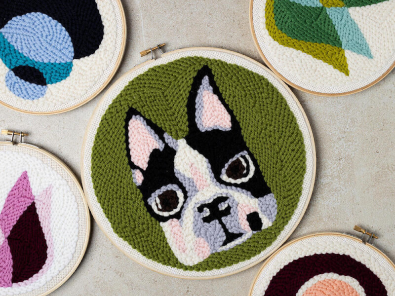 A flatlay image of a selection of embroidery hoops with pug designs in purple, black, white and green