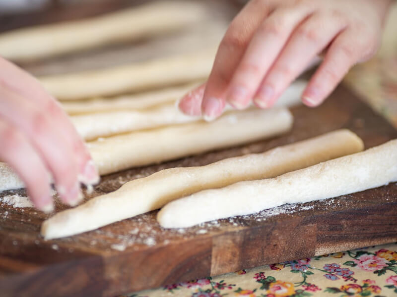 Hands forming gnocchi dough into equal lengths before cutting