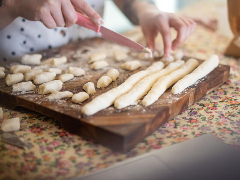 A woman slicing gnocchi at a cooking class.