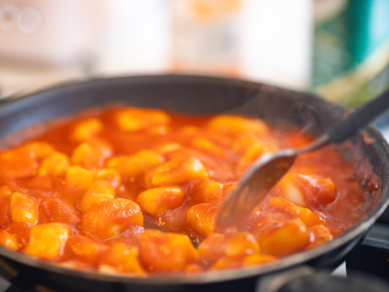 A pan of gnocchi in red sauce being stirred in a pan