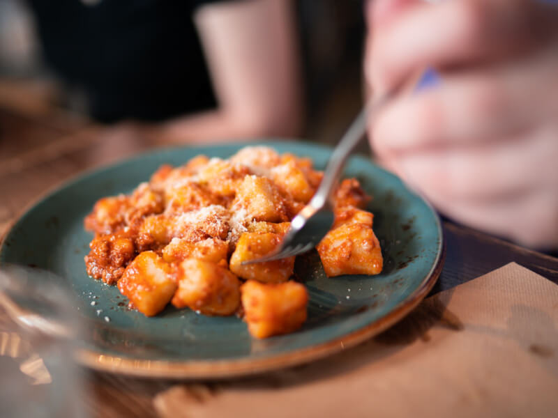 Silver fork digging into a fresh plate of gnocchi sprinkled with parmesan and tomato sauce 