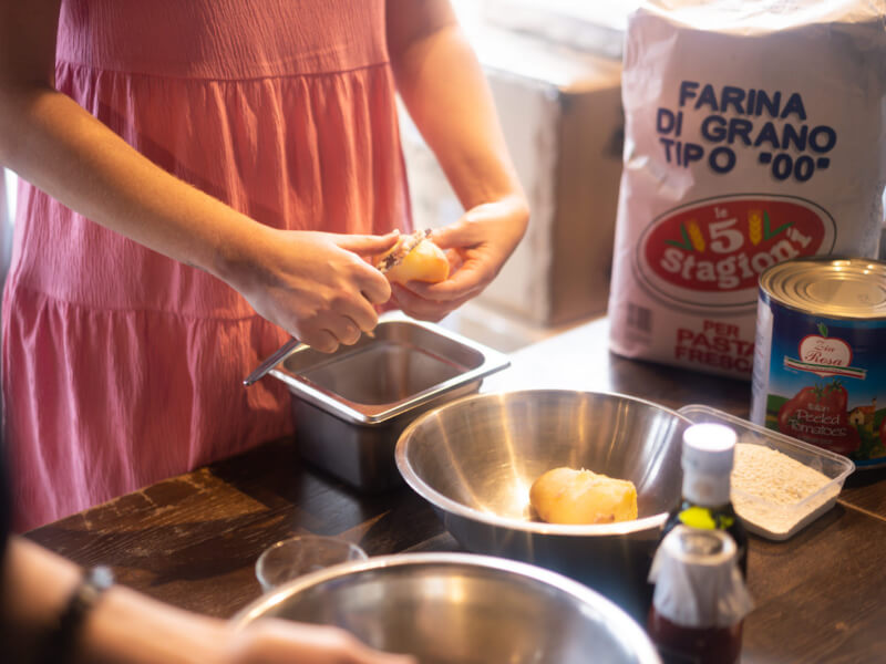 A person preparing fresh gnocchi at a table covered with various ingredients