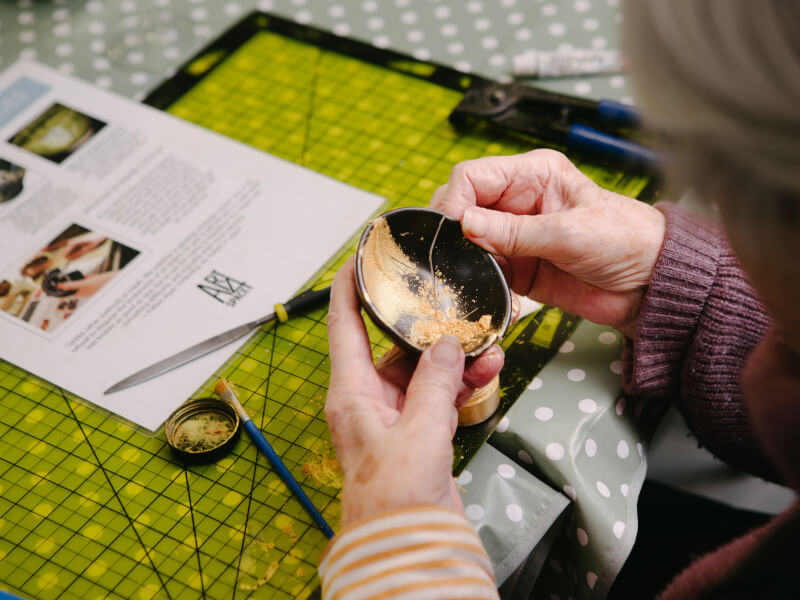 A woman is sitting at a table at a kitsugi class, fixing pottery with gold powder and resin