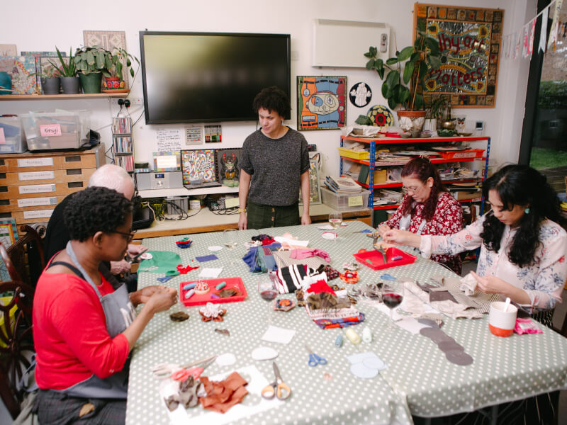 A group of students at a sewing class, sitting around a table covered with materials