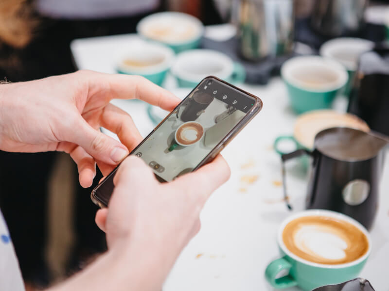 A close up of a person taking a photo of a cup of coffee on a smartphone