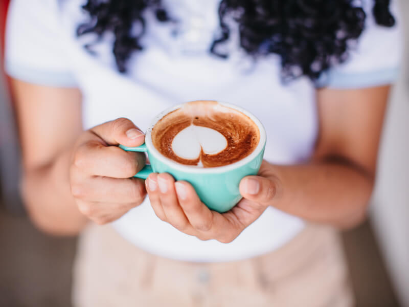 Close up of a person holding a latte with latte art in a turquoise cup