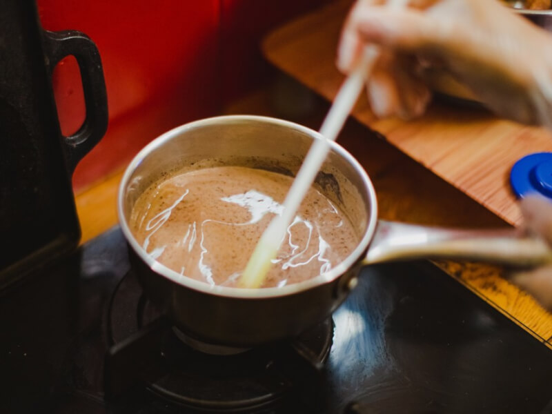 A person stirring a metal pan of melted chocolate