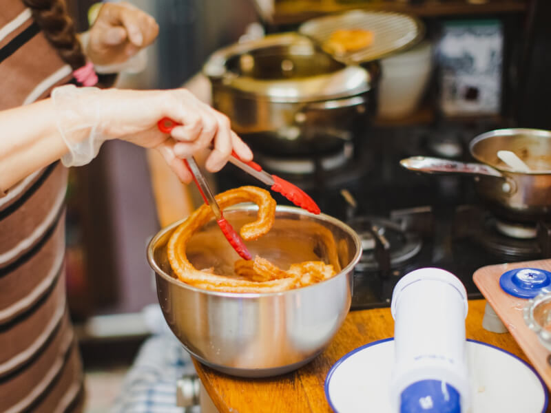 A woman with tongs stirring a metal bowl of fresh churros