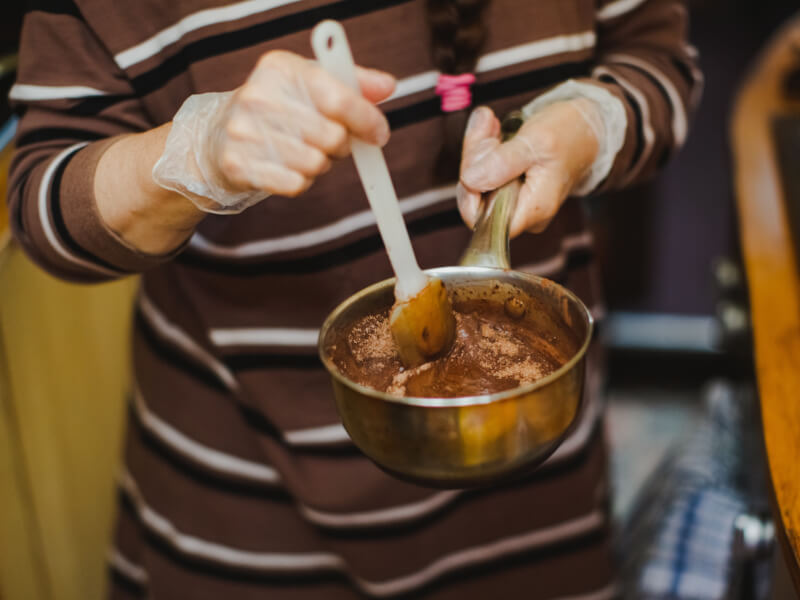 A person in a striped shirt holds a pan of melted chocolate