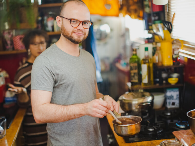 A man in a grey tshirt stands holding a saucepan full of melted chocolate