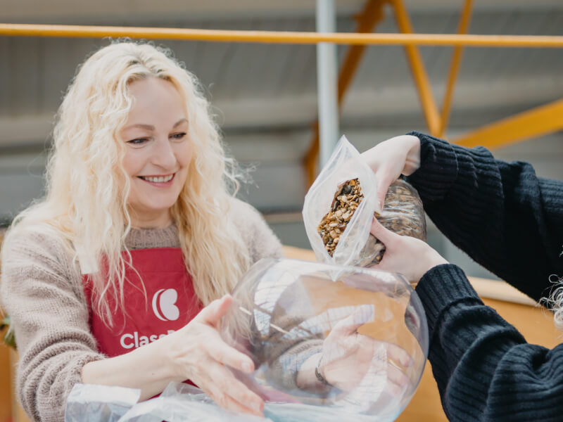 Woman holding a glass terrarium bowl whilst hands pour a bag of pebbles into it for a terrarium base