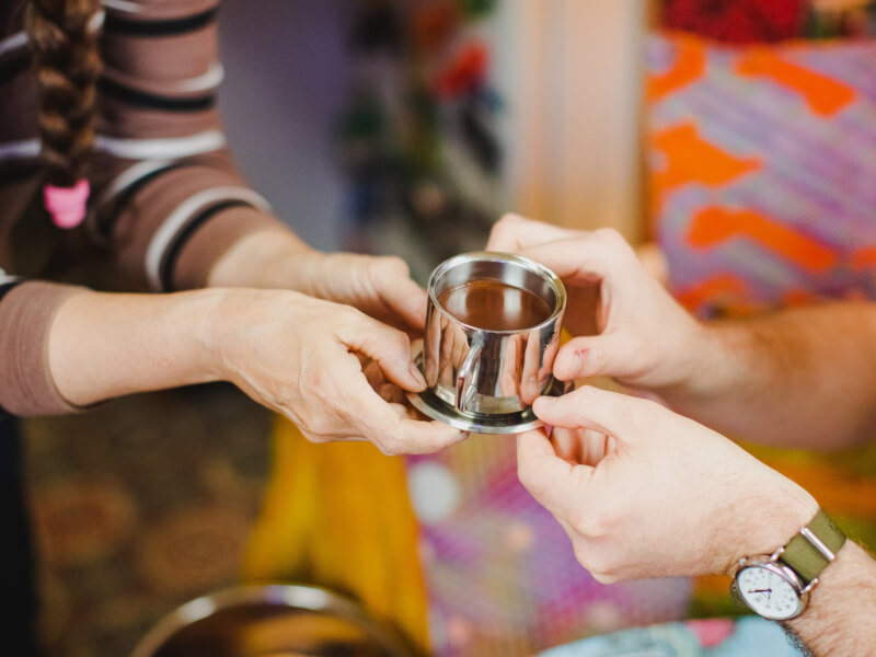Two sets of hands holding a metal cup and saucer full of melted chocolate