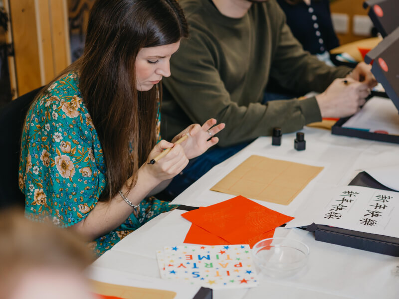 A woman in a floral top sits in front of a variety of papercraft materials