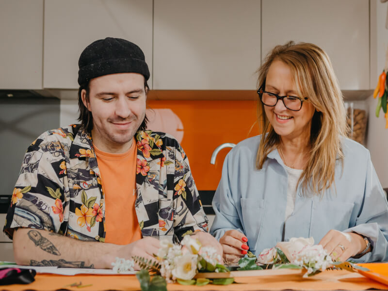 A man and woman sit at a table making a decorative hoop from fresh flowers