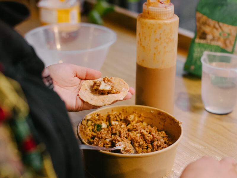 A person is holding a piece of handmade pasta and adding filling to make it into ravioli