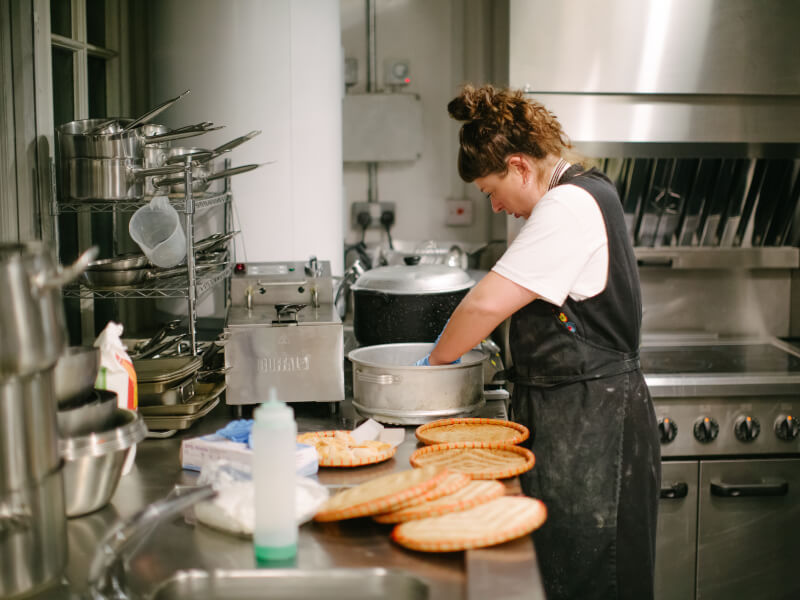 A person standing in a professional kitchen preparing a metal pot for cooking