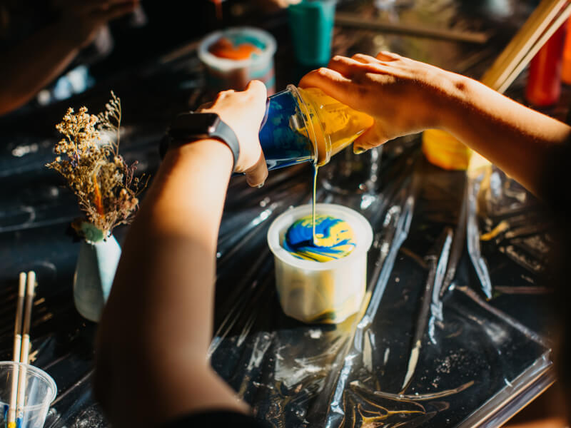 Hands pouring blue and yellow terrazzo formula from plastic tubs into a terrazzo mould to create a swirl pattern