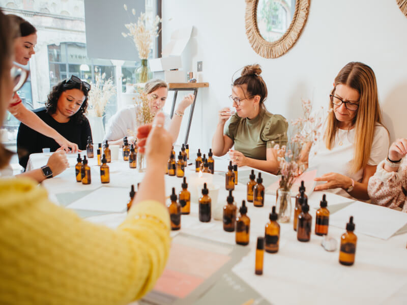 Women sit around a table of perfume ingredients at a perfume making class