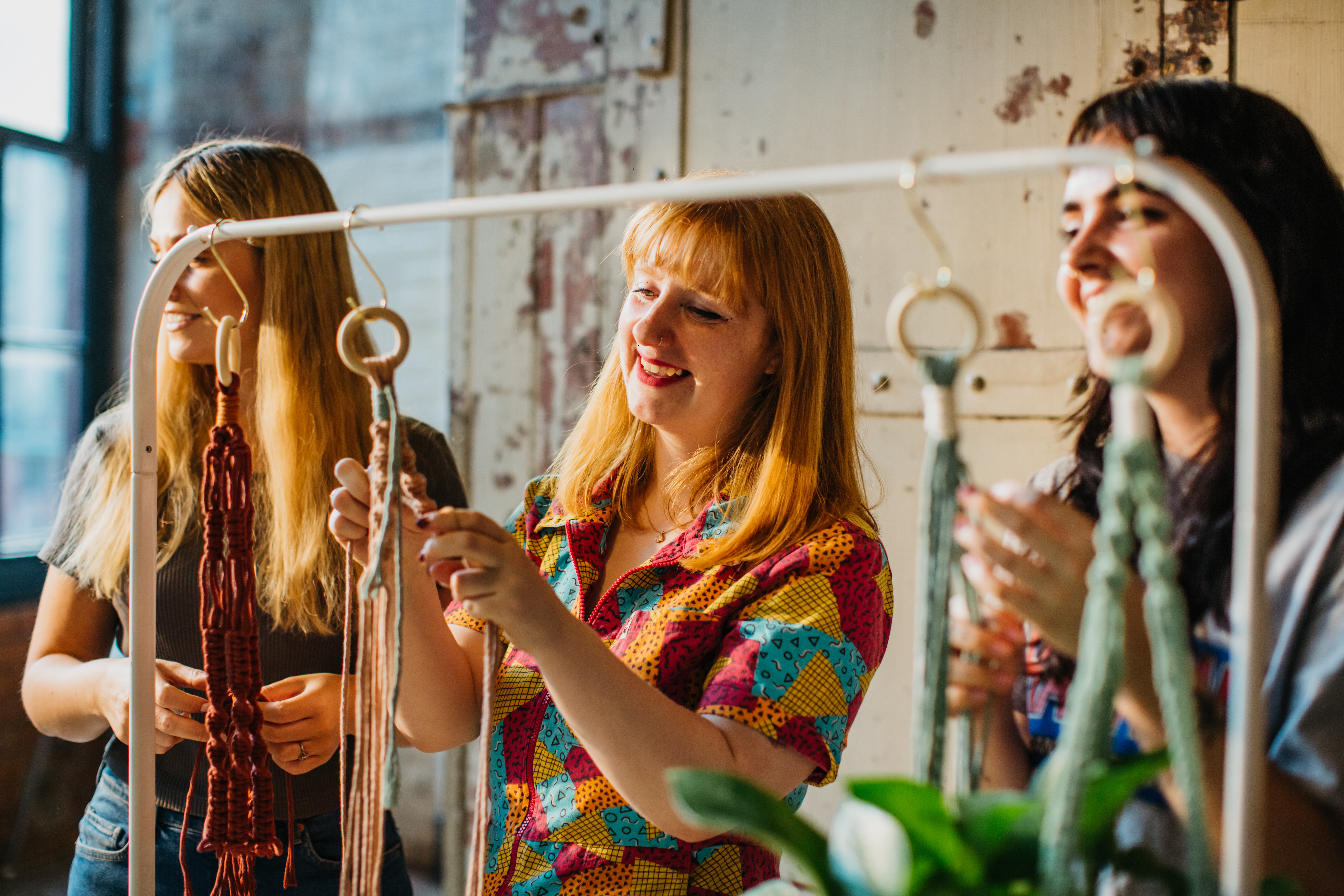 Three people smile as they learn how to macrame.