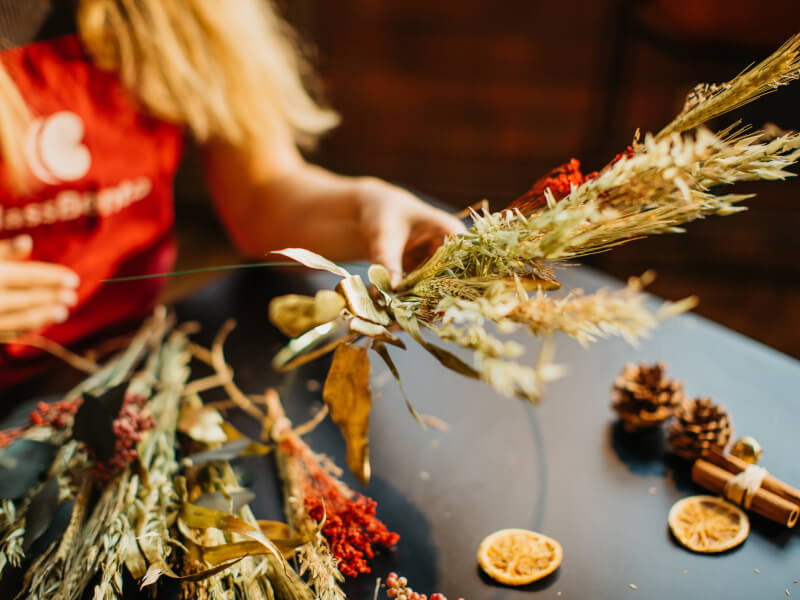 A hand selecting dried foliage from a selection of white and red tones for a Christmas wreath
