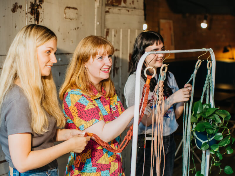 Three women smiling whilst making macrame plant hangers. 
