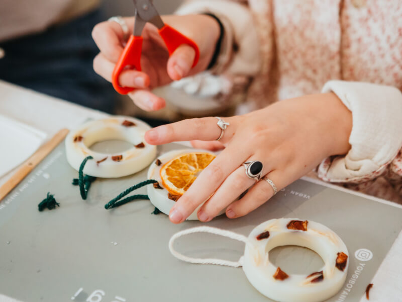 A close up of a person cutting string to add to eco Christmas decorations, made with wax and dried fruits