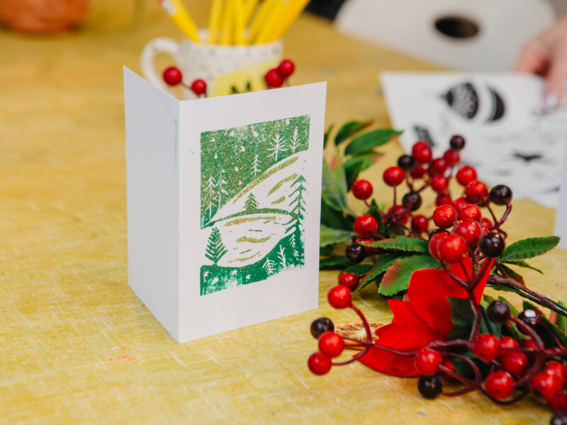 Close up of a block-printed Christmas card on a table with Christmas decorations
