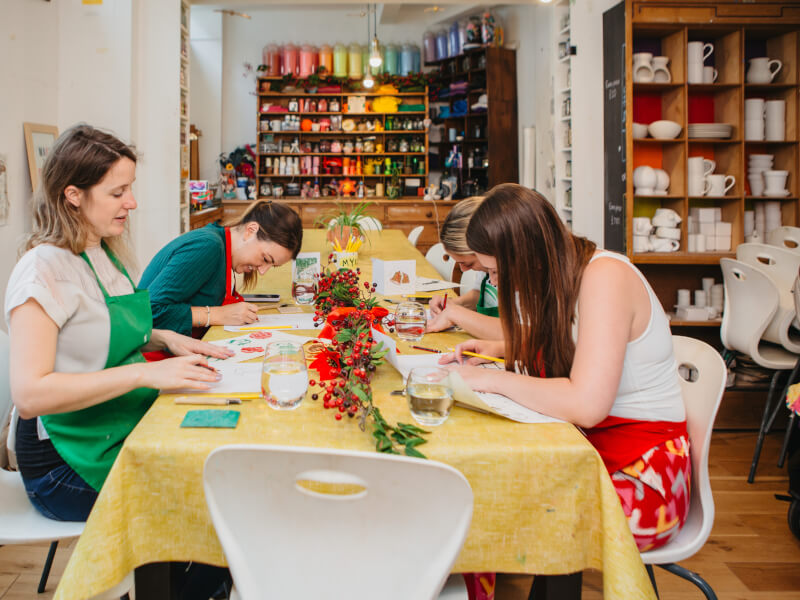 Four women sit at a table at M.Y.O studio at a lino printing Christmas card class