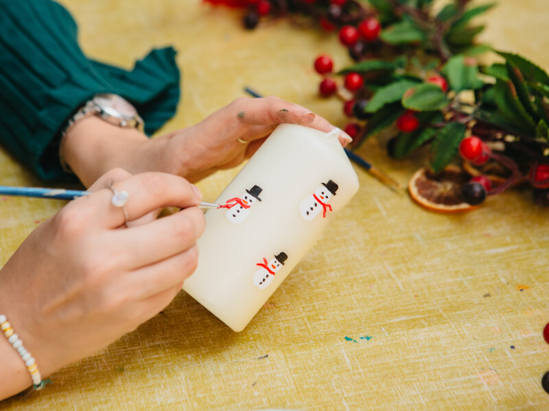 A close up shot of someone painting a candle with snowmen motifs