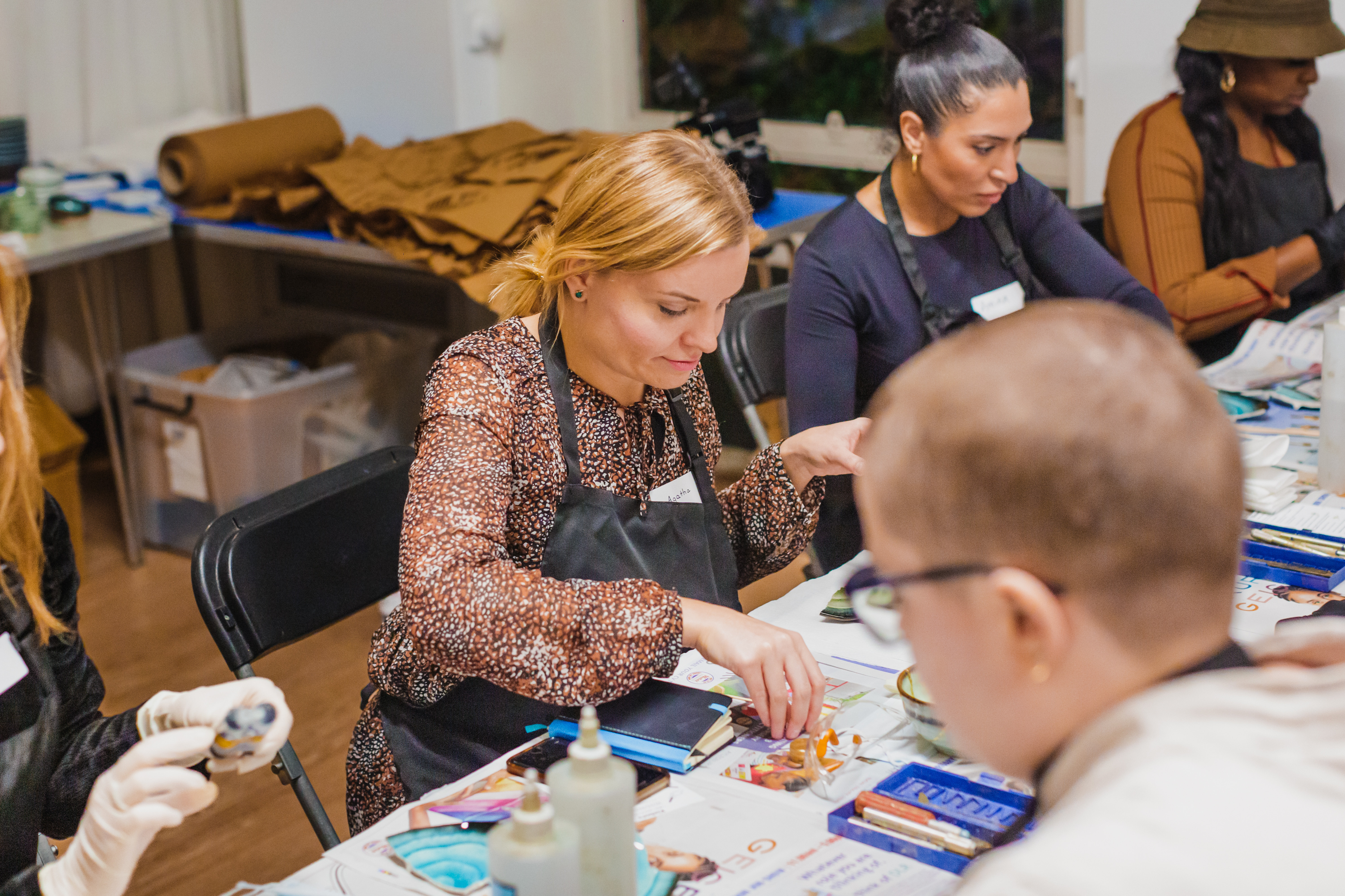 A woman sits at a table with other participants in a pottery class