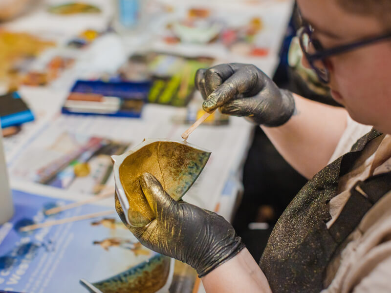 A person is applying gold adhesive to a broken piece of pottery at a kintsugi class