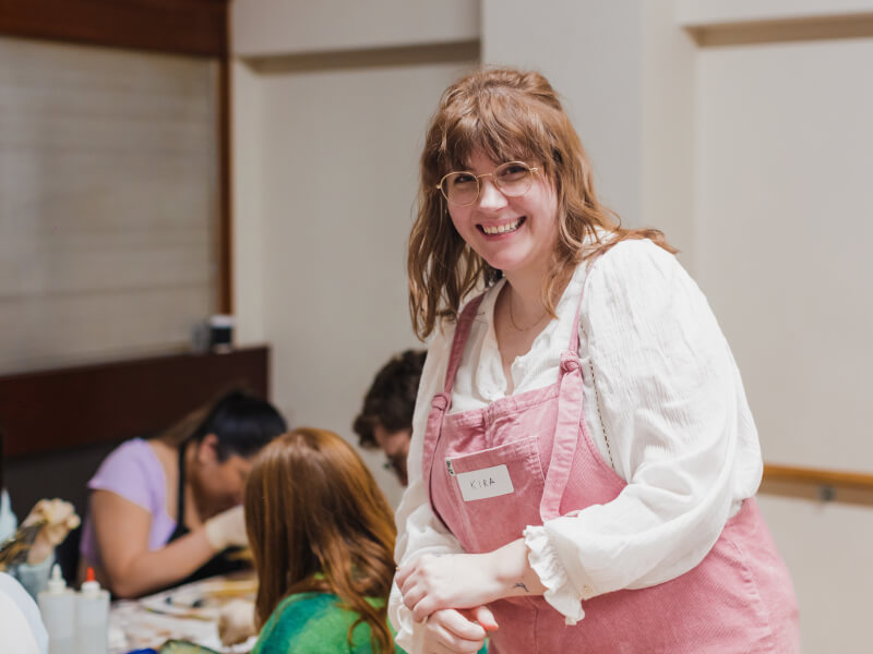 Woman wearing a pink apron smiling at a craft class in Manchester.