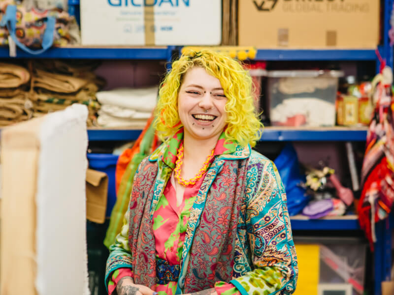 A person with colourful hair smiles as she teaches a tufting class