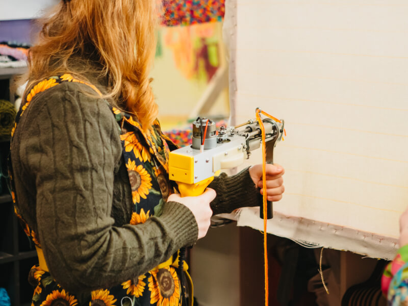 A person wearing sunflower-printed clothes uses a tufting gun
