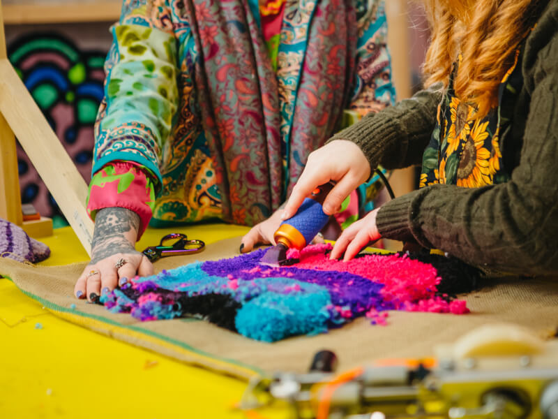 A close up of two women trimming a colourful tufted project
