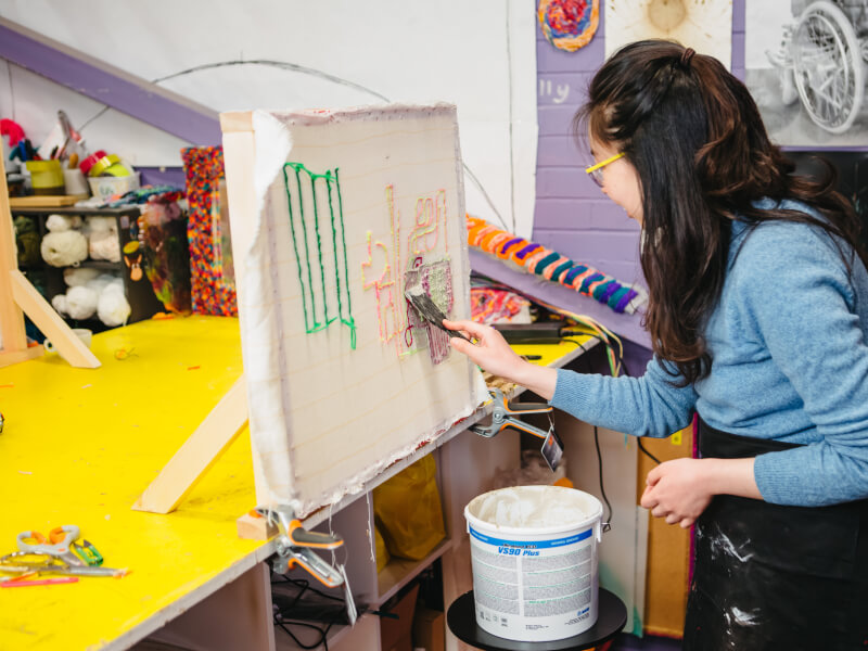 Person using a paintbrush to apply fixative to their tufting project