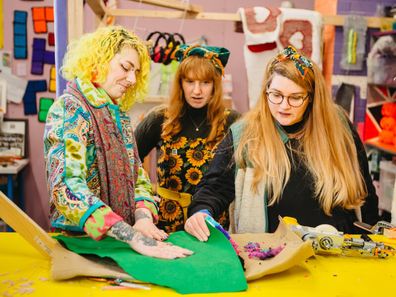 Three colourfully-dressed people enjoy their tufting class together