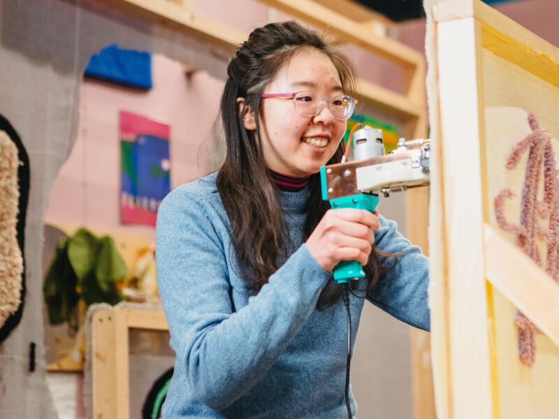 Person smiling as they enjoy a tufting class