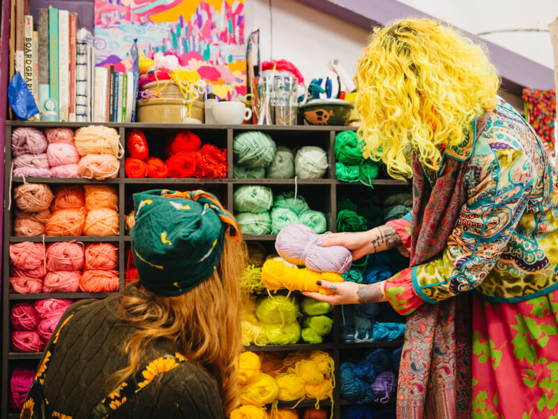 Two women looking at balls of yarn on a shelf at a craft class.