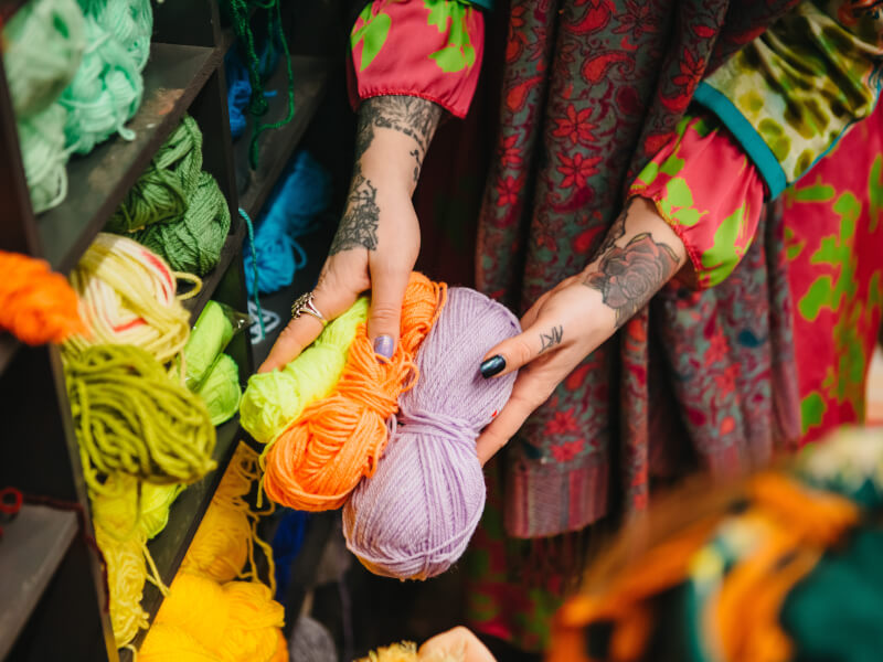 A person picks knitting yarn skeins from a few colourful options.