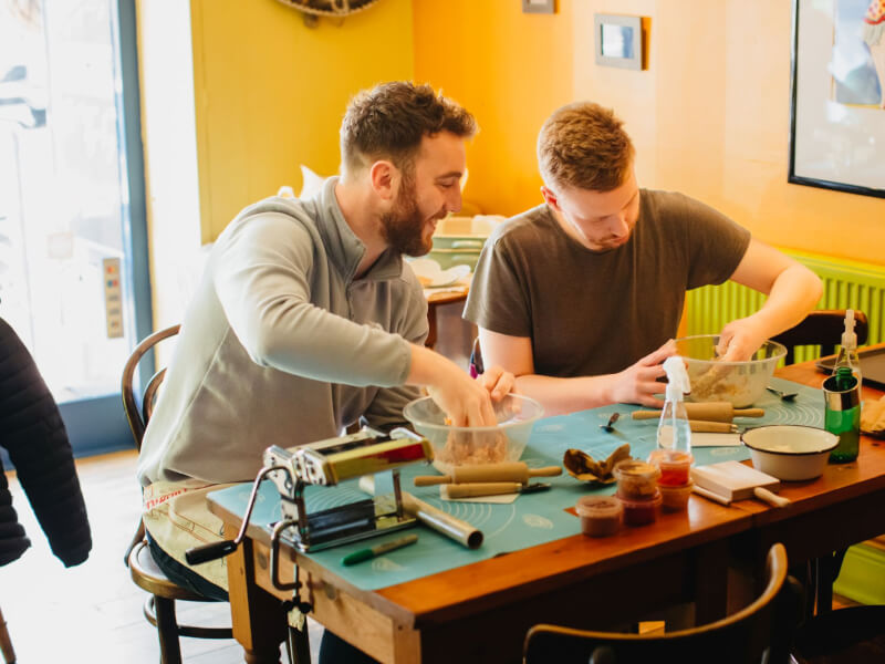 Two men sit side by side at a pasta making class