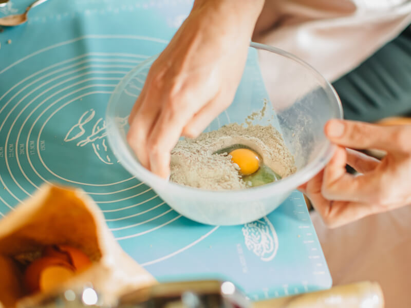 Person mixing egg and flour in a plastic mixing bowl
