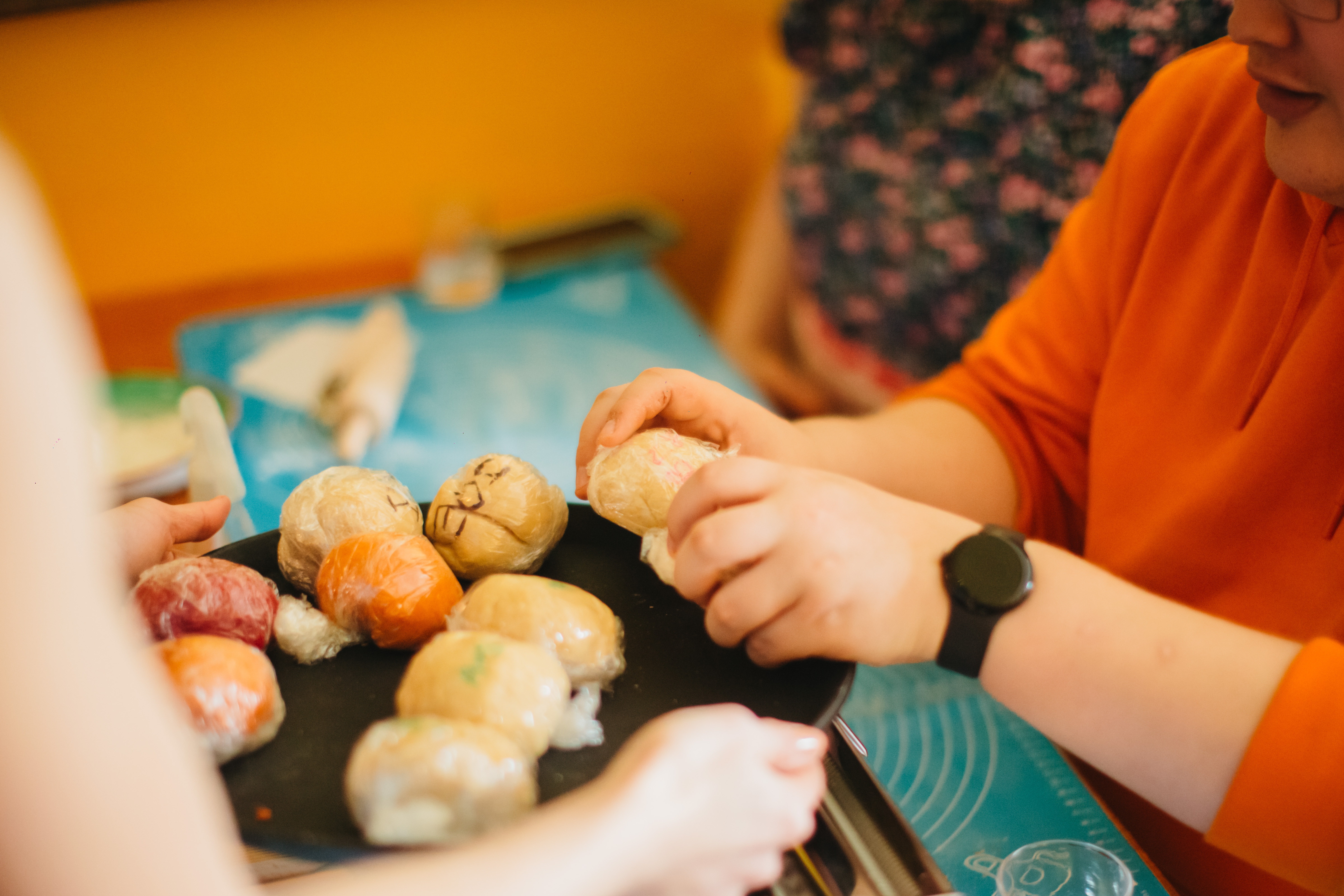Person holding a tray with plastic-wrapped pieces of pasta dough for another person to choose from